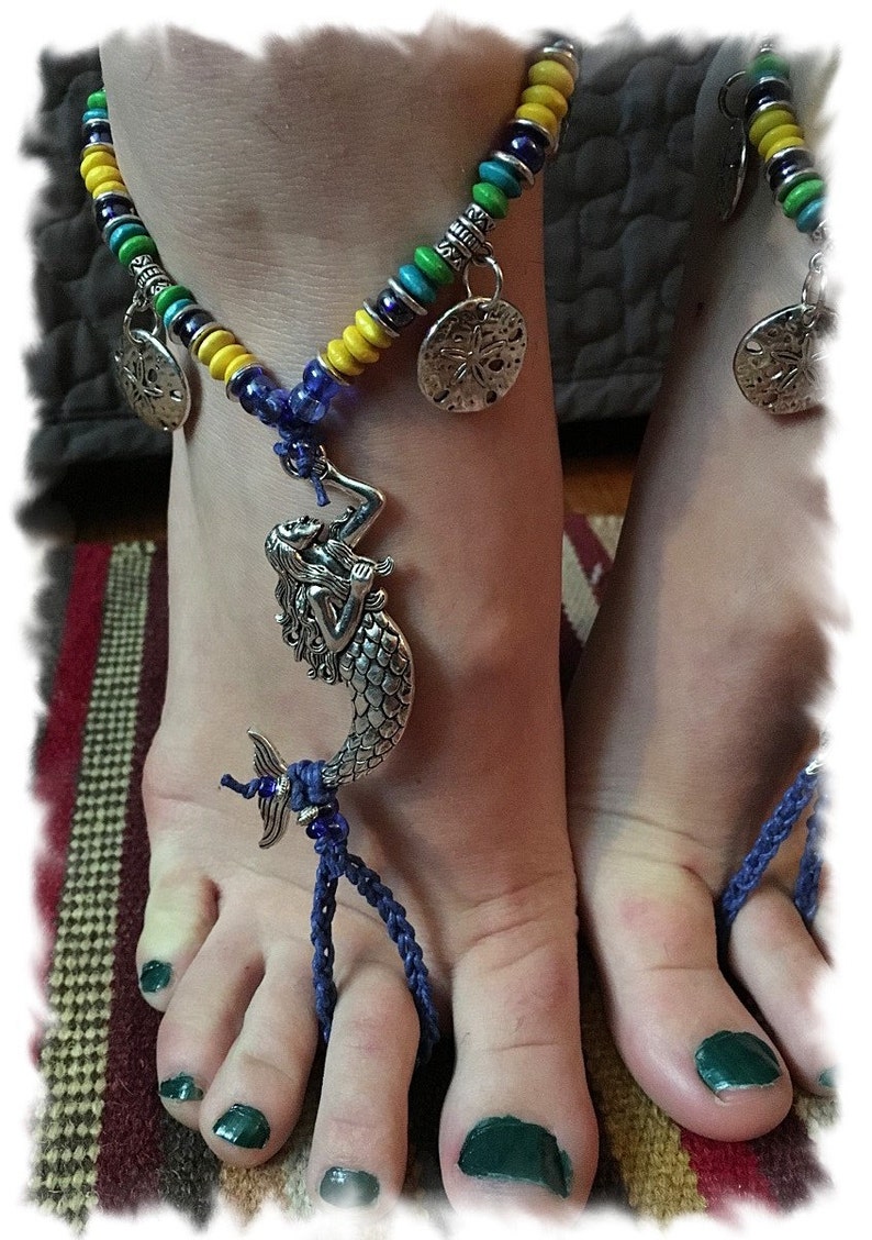 May include: A blue and yellow beaded anklet with a mermaid charm and two starfish charms. The anklet is worn on a person's foot with green nail polish.