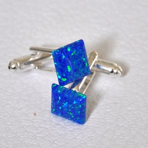 May include: A pair of silver cufflinks with square blue opal stones. The opals have a green and blue iridescent shimmer.