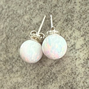 May include: A pair of stud earrings featuring round, white opal cabochons with iridescent flashes of pink, blue, and green. The stones are set in silver-toned metal posts with matching butterfly clutch backings, showcasing a smooth, polished finish.