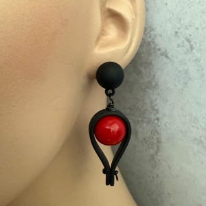 Peut inclure: Boucles d'oreilles pendantes noires avec une boule rouge au centre du pendentif. Les boucles d'oreilles sont en pâte polymère.