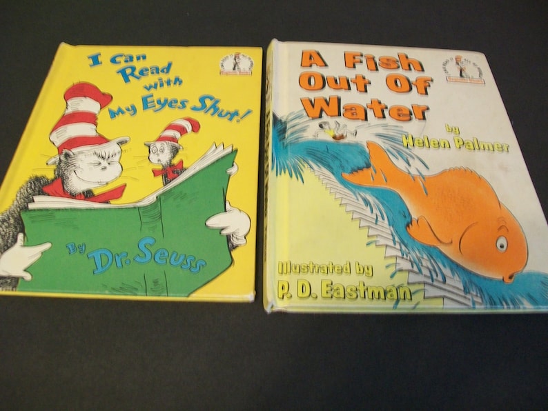 May include: Two children's books, one titled "I Can Read with My Eyes Shut!" by Dr. Seuss, featuring a cat in a red and white striped hat reading a green book, and the other titled "A Fish Out Of Water" by Helen Palmer, illustrated by P.D. Eastman, featuring a goldfish jumping out of water.