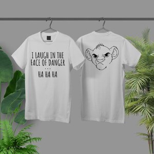 Peut inclure: T-shirt blanc avec un graphique de visage de lion au dos et le texte "I laugh in the face of danger... HA HA HA" sur le devant.