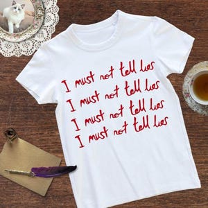 Może przedstawiać: Biała koszulka z napisem "I must not tell lies" napisanym cztery razy na czerwono.