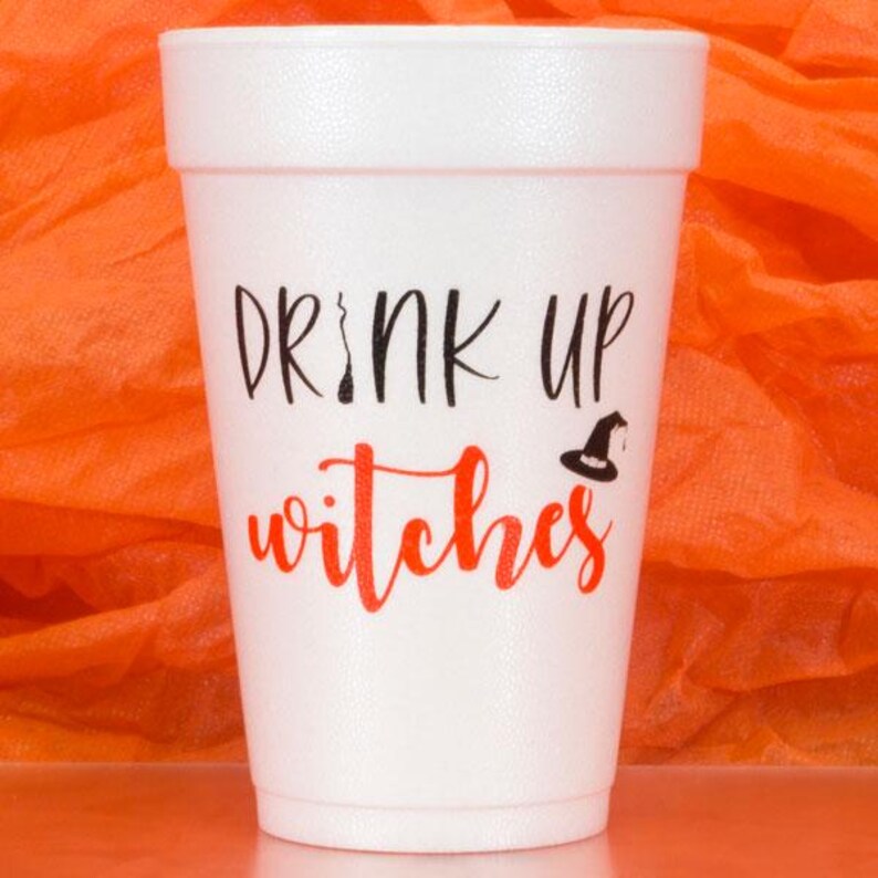 May include: A white foam cup with the phrase "DRINK UP witches" in black and red lettering, with a witch hat graphic. The cup is set against an orange background, suggesting a Halloween theme.