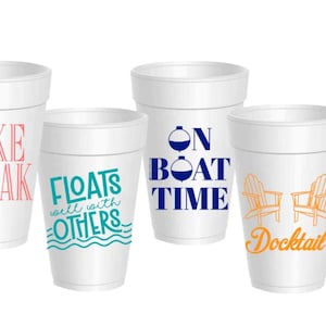 May include: Four white foam cups with various designs. One cup has "Lake Break" in pink, another says "Floats well with others" in teal, a third says "On Boat Time" in blue, and the last says "Docktail" with orange Adirondack chairs.