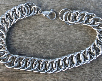 May include: A silver chain bracelet with a lobster clasp closure. The chain is made of interlocking metal rings.