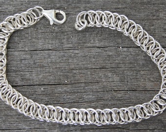 May include: A silver chain bracelet with a lobster clasp closure. The chain is made of interlocking rings.