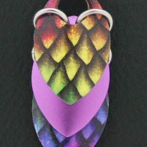 May include: A pair of earrings with a heart-shaped design. The heart is made of three layers of polymer clay, each with a different pattern. The top layer is a rainbow pattern, the middle layer is a solid purple, and the bottom layer is a purple and black pattern. The earrings are attached to silver hooks.