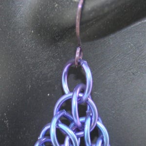 May include: A pair of earrings made of interwoven metal rings in a blue and purple iridescent finish.