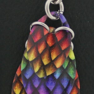 May include: Rainbow colored dangle earrings with a layered, scale-like design. The earrings are made of metal and have a silver finish.
