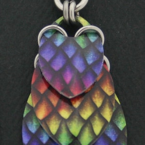 May include: Rainbow colored dangle earrings with a layered, scale-like design. The earrings are made of metal and have a silver hook.