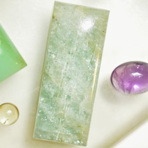 May include: A rectangular, light green aquamarine gemstone with a smooth, polished surface. The gemstone has a translucent appearance with visible internal inclusions.