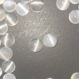 May include: A close-up of a group of white, round, iridescent stones. The stones are arranged in a semi-circle on a dark grey surface.