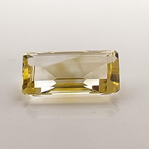 May include: A clear, faceted, rectangular gemstone with a yellow hue. The gemstone is cut in a step-cut style.