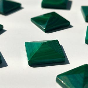 May include: A collection of eight green malachite pyramid-shaped stones on a white surface.