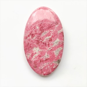 Peut inclure: Pierre précieuse de forme ovale et à surface polie. La pierre présente une teinte rose vif avec des motifs complexes de veinures grises et blanches. La pierre mesure environ 5 cm de long.