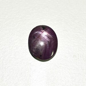 May include: A round, purple gemstone with a star-like pattern. The gemstone has a smooth, polished surface.