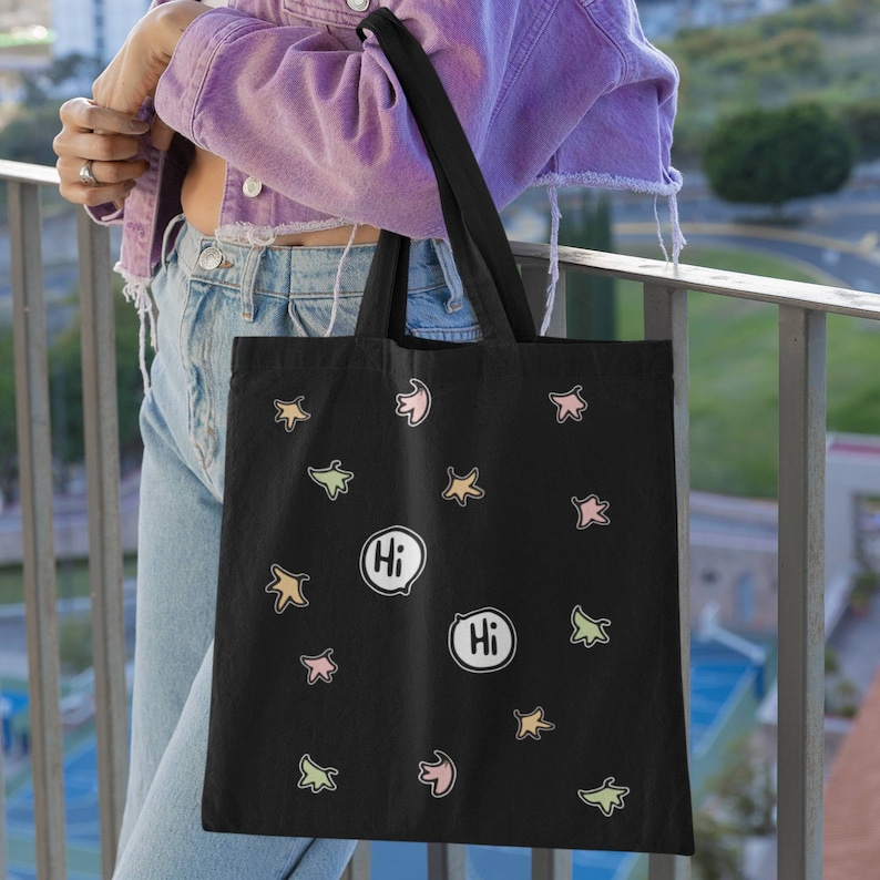 Heartstopper Leaves Tote Bag in Black on arm of lady. Heartstopper leaves printed on both sides of the bag along with two Hi quotes from the show.