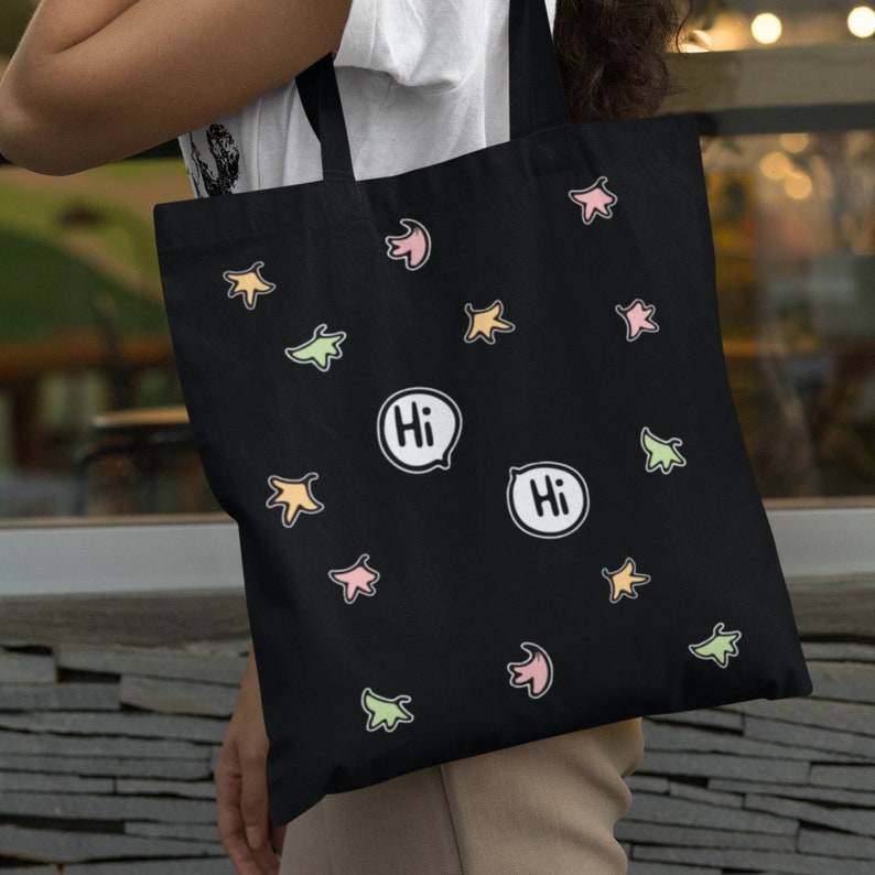 Heartstopper Leaves Tote Bag in Black Cotton on arm of lady. Heartstopper leaves printed on both sides of the bag along with two Hi quotes from the show.