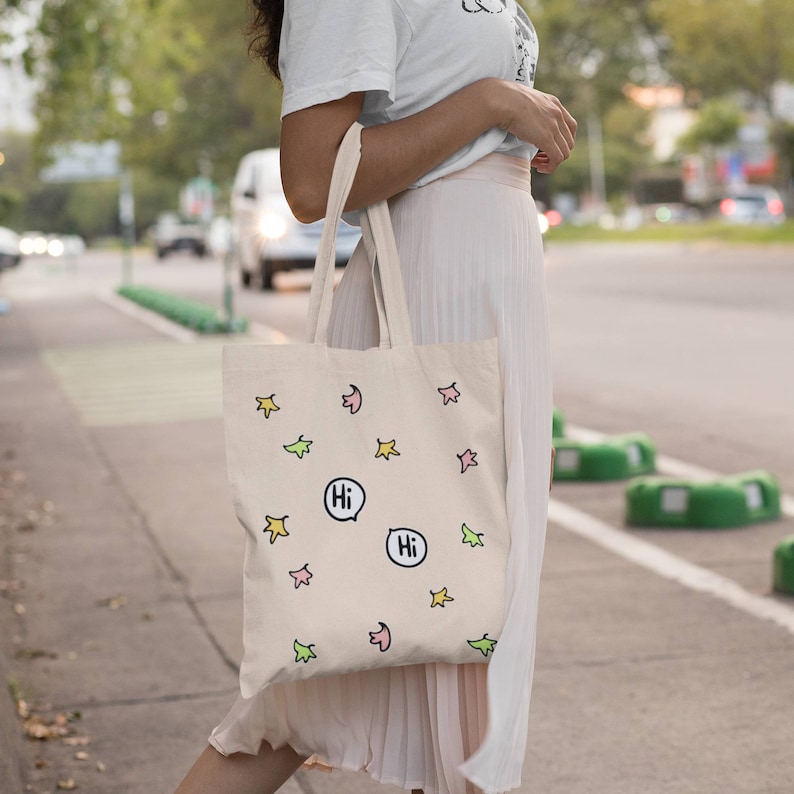 Heartstopper Leaves Tote Bag in Natural Cotton on arm of lady. Heartstopper leaves printed on both sides of the bag along with two Hi quotes from the show.