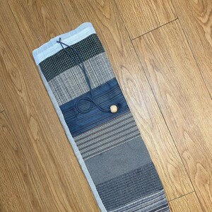 May include: A gray and blue yoga mat bag with a drawstring closure and a wooden toggle. The bag is made of a woven fabric with a variety of patterns.