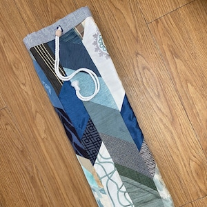 May include: A blue and white patchwork yoga mat bag with a drawstring closure. The bag is made of various fabrics with different patterns and textures.