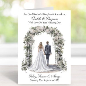 Puede incluir: Una tarjeta de boda con una ilustraci&oacute;n de acuarela de una pareja caminando bajo un arco floral. La tarjeta dice "For Our Wonderful Daughter & Son in Law Charlotte & Benjamin With Love On Your Wedding Day Today. Forever & Always Saturday 23rd September 2023"