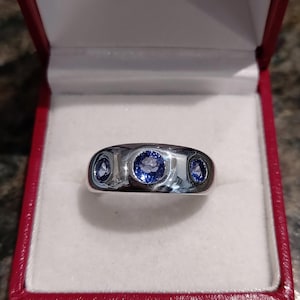 Puede incluir: Un anillo de plata con tres piedras preciosas azules engastadas en una banda lisa.