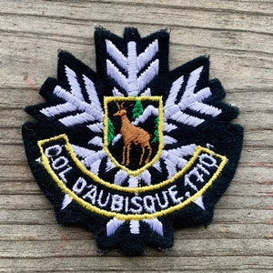 May include: Black embroidered patch with a white snowflake design, a yellow border, and the text "Col d'Aubisque 1709". A green and brown deer is in the center of the patch.