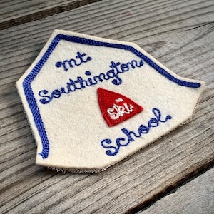 May include: White felt patch with blue embroidered border. The patch features the text "Mt. Southington Ski School" in blue embroidery. A red embroidered triangle with the word "Ski" inside is centered above the text.