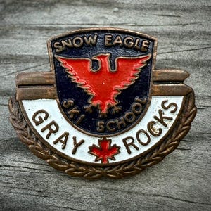 May include: Vintage Snow Eagle Ski School pin. The pin features a red eagle on a navy blue background, with the words "Snow Eagle Ski School" and "Gray Rocks" in white lettering. A red maple leaf is also present.