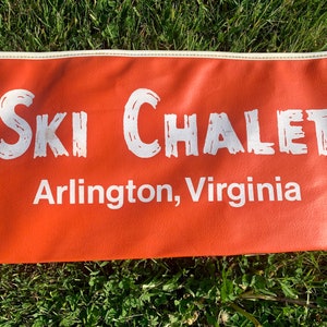 May include: Orange fabric banner with white text that reads "Ski Chalet Arlington, Virginia".