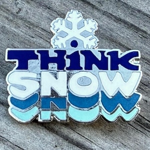 May include: A silver-toned pin with the words "THINK SNOW" in blue and white, topped with a snowflake. The pin has a winter theme, with a light blue and silver color scheme.