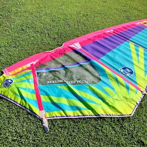 May include: A colorful windsurfing sail with a pink, purple, blue, green, and yellow design. The sail has the text "Slalom Speed TCC4" printed on it.