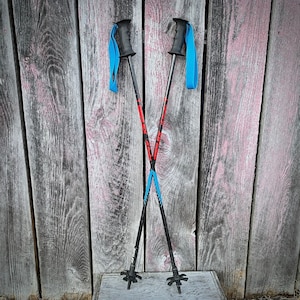 May include: A pair of black ski poles with red and blue accents, crossed and leaning against a wooden wall.