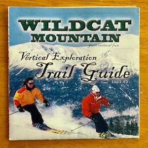 May include: A Wildcat Mountain Trail Guide from 2002-03. The cover features skiers on a snowy mountain slope under a blue sky. The guide's title is in large green letters, with the words "pure vertical fun" below. The words "Vertical Exploration" and "Trail Guide" are also visible.