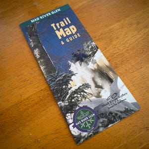 May include: A folded brochure titled "Trail Map & Guide" for Mad River Glen, featuring a skier in action. The brochure has a green and white logo with the text "Mad River Glen Since 1949". The background shows a snowy mountain scene.