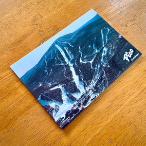 May include: A vintage postcard featuring an aerial view of Pico Mountain in Vermont. The postcard shows the ski slopes and trails winding through the snow-covered mountainside. The text "Pico in Vermont" is printed in the bottom right corner.