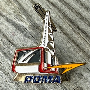 May include: A metal lapel pin featuring a stylized cable car and support tower design in white, red, black, and gold enamel. The pin includes a prominent yellow arrow graphic pointing right and the word POMA in bold blue capital letters at the base.