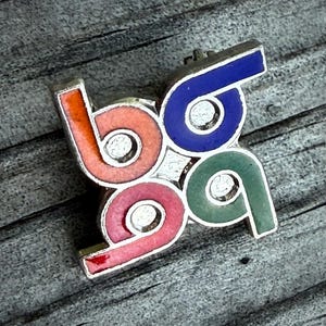 May include: A colorful enamel pin with the numbers "69" in a repeating pattern. The pin features the numbers in orange, pink, green, and blue, with a silver border. The pin is a unique accessory.