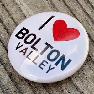 May include: White button with black text that reads "I love Bolton Valley" and a red heart.