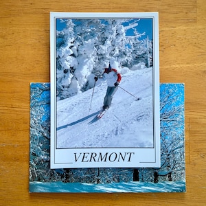 May include: A postcard featuring a snowy landscape with a skier in a red and white jacket skiing down a slope. The postcard says "VERMONT" at the bottom.