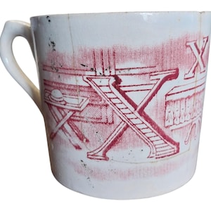 May include: White ceramic mug with a red and white design. The design features a stylized letter X and a table with a hat on top.