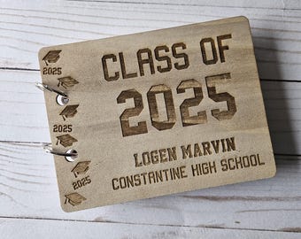 Pode incluir: Uma lembrança de formatura em madeira com o texto "CLASS OF 2025" e o nome "LOGEN MARVIN" e "CONSTANTINE HIGH SCHOOL" gravados. A lembrança de madeira tem uma cor marrom clara e apresenta desenhos de chapéus de formatura.