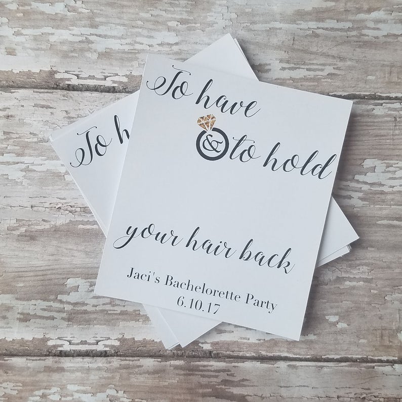 May include: White cards with black calligraphy text that reads "To have & to hold your hair back". A gold diamond ring graphic is above the text. The text "Jaci's Bachelorette Party 6.10.17" is at the bottom.
