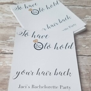 May include: White cards with black script text that reads "To have & to hold your hair back." A diamond ring graphic is above the text. The bottom of the card reads "Jaci's Bachelorette Party 6.10.17."