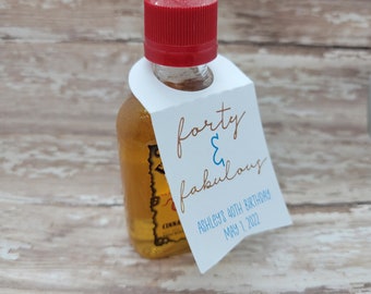 Könnte beinhalten: Eine kleine Flasche mit rotem Verschluss und einem weißen Anhänger mit der Aufschrift "forty & fabulous". Der Anhänger enthält auch "Ashley's 40th Birthday May 1 2022". Die Flasche enthält eine hellbraune Flüssigkeit.