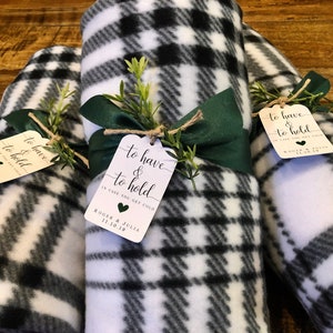 May include: Rolled black and white plaid fleece blankets tied with green ribbon and twine, adorned with tags that read "to have & to hold". The tags also include the text "in case you get cold" and a date.