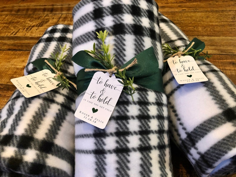 May include: Rolled black and white plaid fleece blankets tied with green ribbon and twine, adorned with tags that read "to have & to hold". The tags also include the text "in case you get cold" and a date.