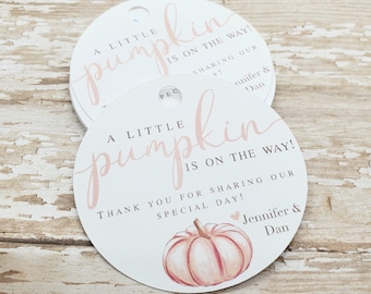 May include: Round white tags with the text "A LITTLE pumpkin IS ON THE WAY!" in pink script. A watercolor pumpkin illustration is at the bottom. The tags are for a baby shower, with the names Jennifer & Dan.